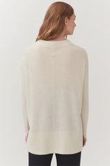 Woman standing, viewed from back, wearing a long-sleeved top and pants.