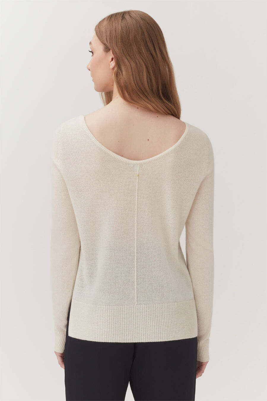 Woman standing, seen from behind, wearing a sweater with a zipper down the back.