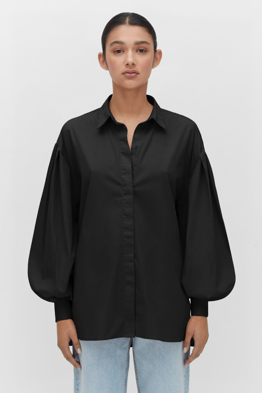 Woman in a buttoned shirt and jeans standing straight