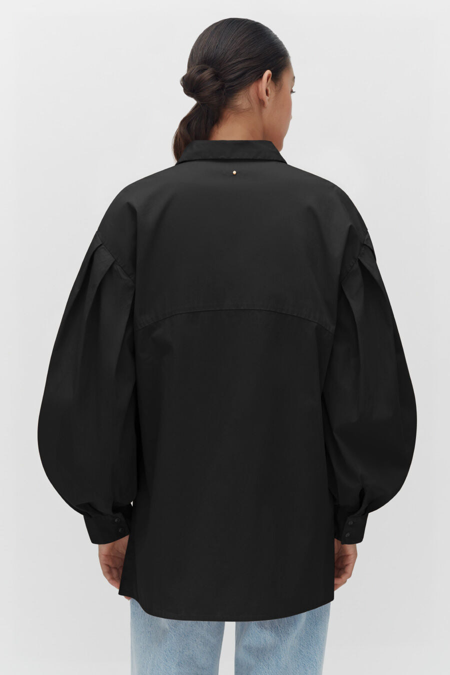 Person viewed from behind wearing a loose shirt and jeans.