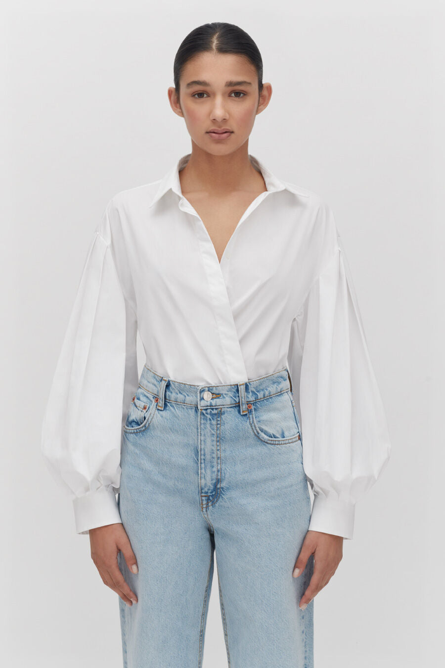 Woman in a blouse and jeans standing with hands at her sides.