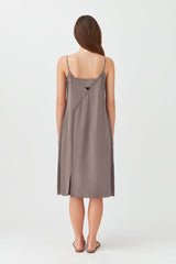 Woman viewed from back wearing a knee-length dress, standing against a plain background.