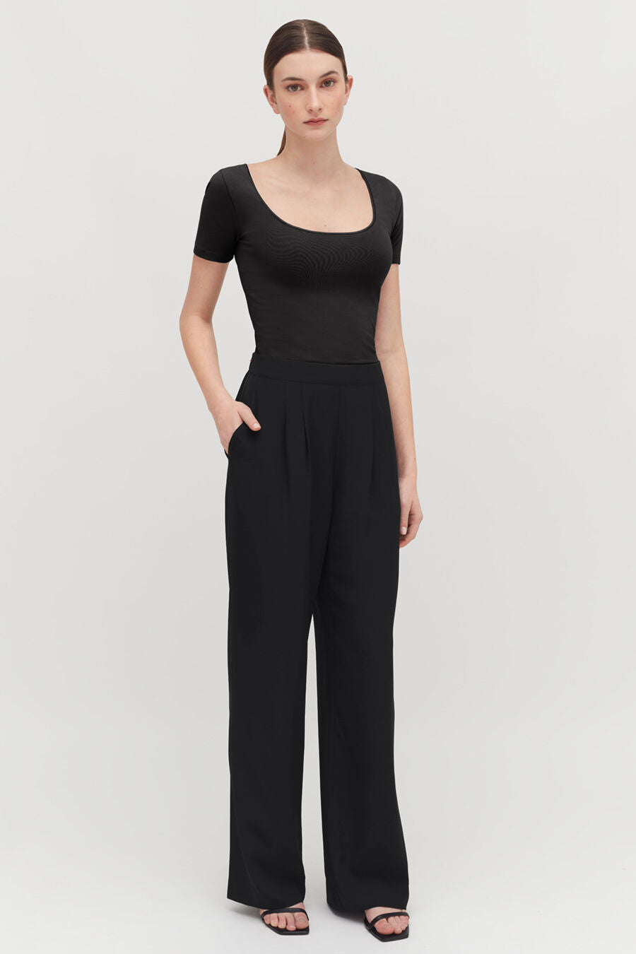 Woman standing in a short-sleeve top and trousers, hands on hips.