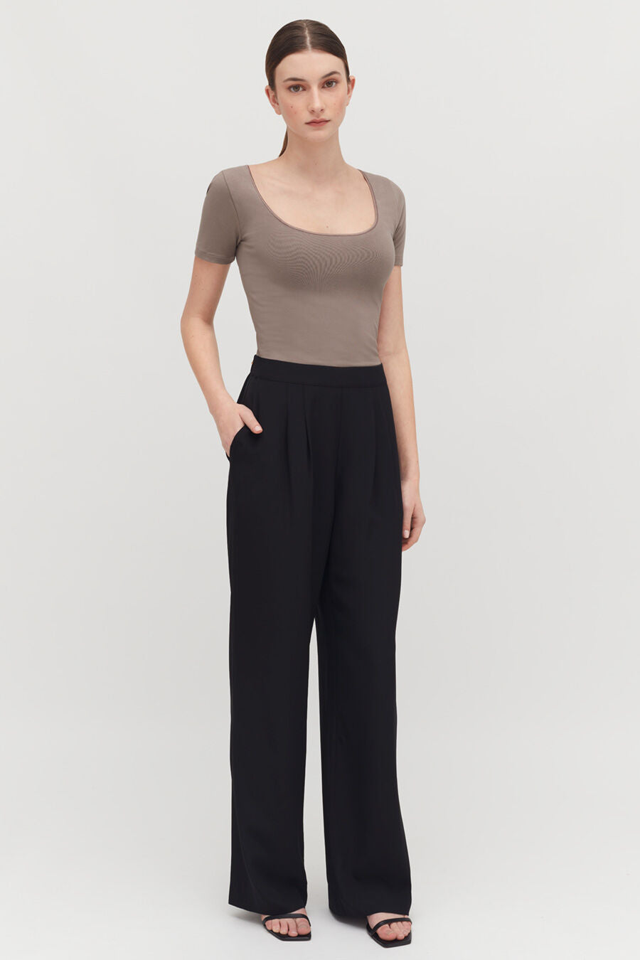 Woman standing in a fitted top and loose pants, hands on hips.