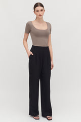 Woman standing in a fitted top and loose pants, hands on hips.
