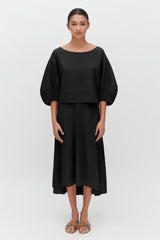 Woman in a blouse and skirt standing straight, facing forward.