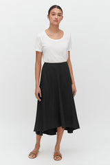 Woman in a T-shirt and mid-length skirt standing straight with sandals.