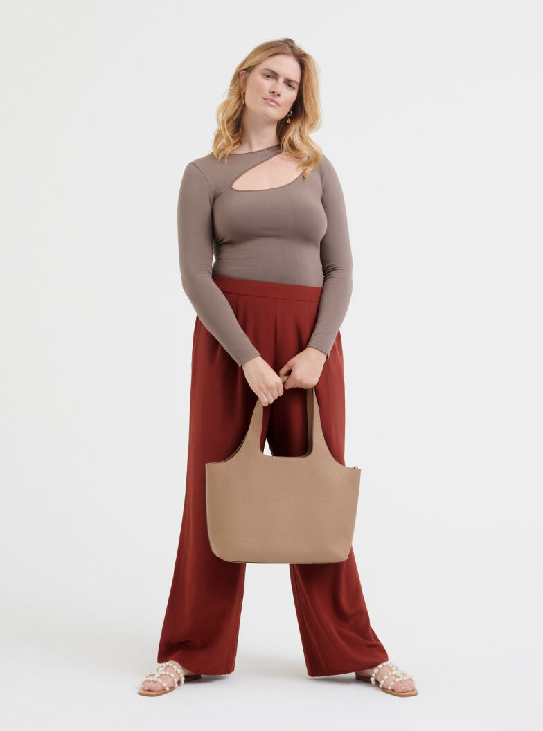 Woman standing with a handbag and wearing a long-sleeve top and wide-leg pants.