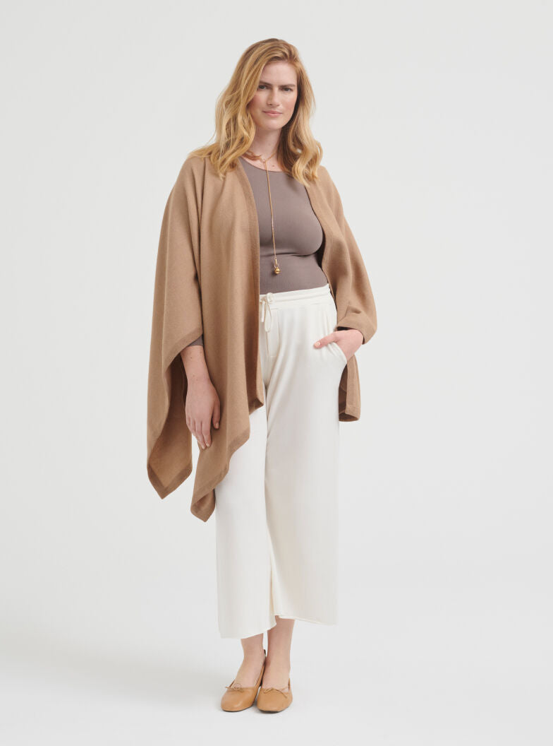 Woman standing in a studio wearing a flowing top, pants, and shoes.