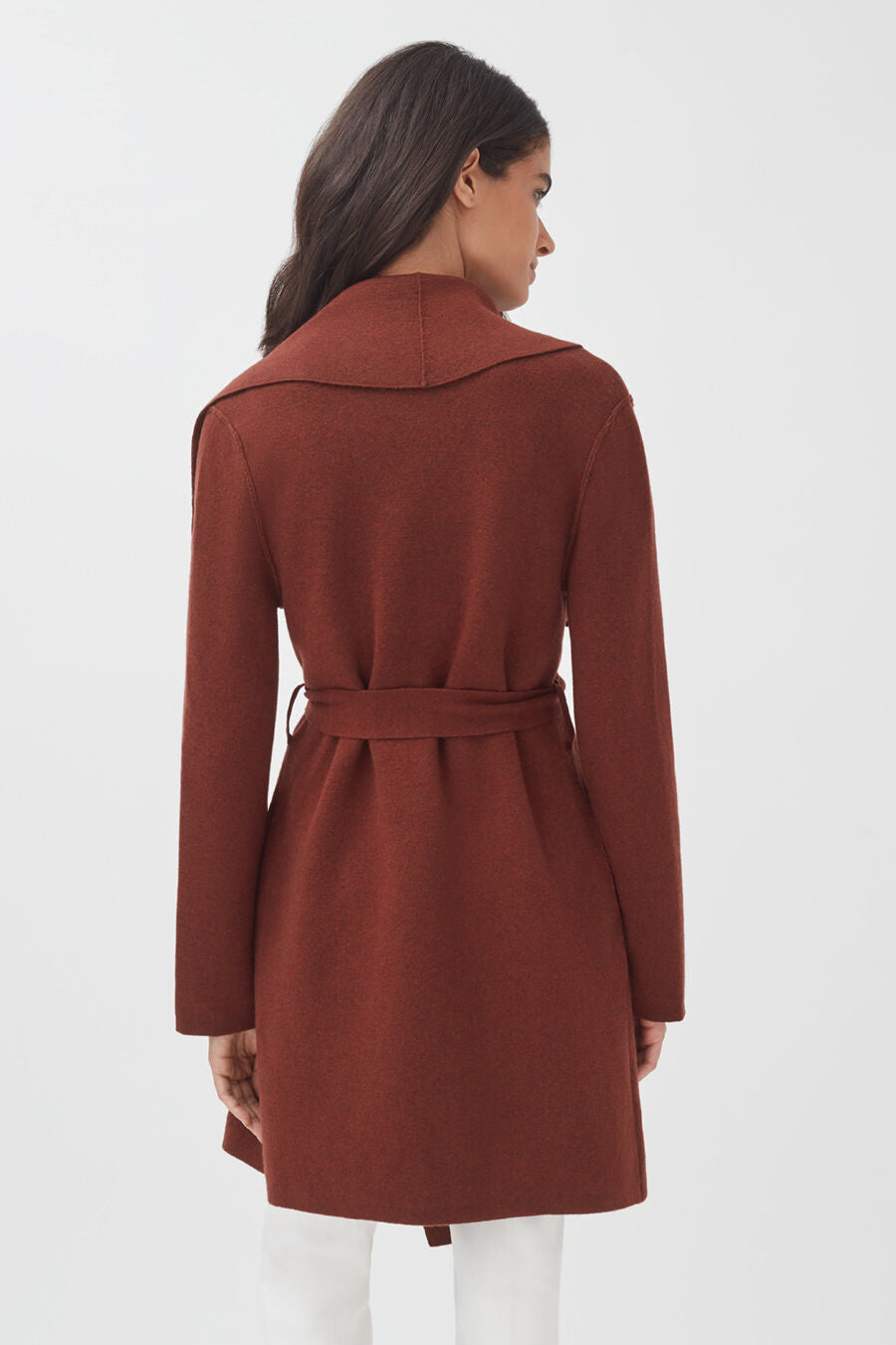 Woman standing with her back facing the camera, wearing a belted coat.