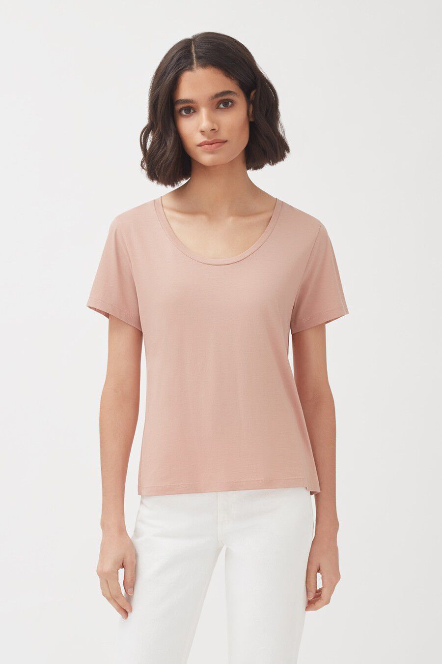 Woman in a plain t-shirt and pants standing against a white background.
