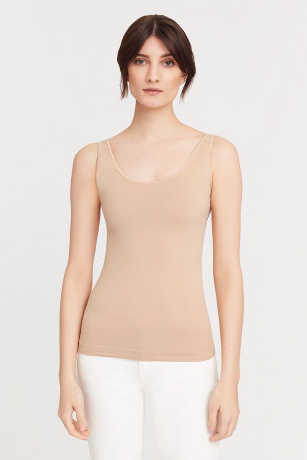 Woman in a sleeveless top and white pants standing and facing the camera.