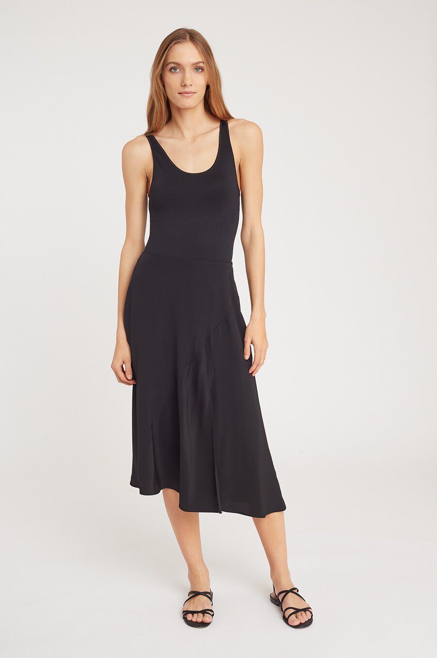 Woman in a sleeveless top and skirt stands against a light background.